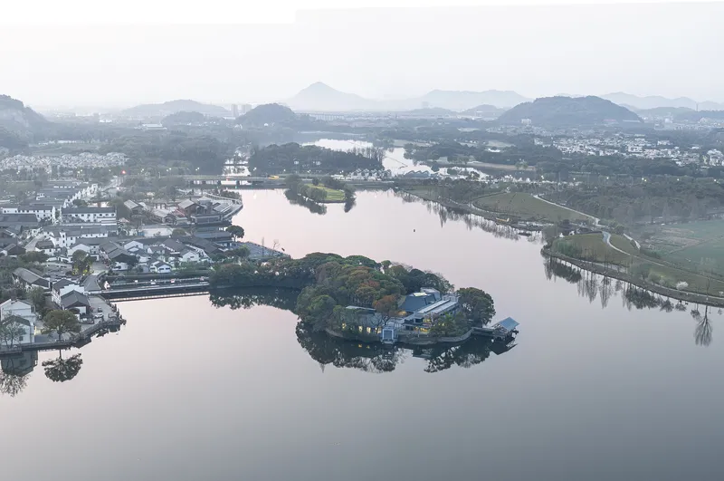 Wide aerial view of the island pavilion within the lake and surrounding village in morning mist