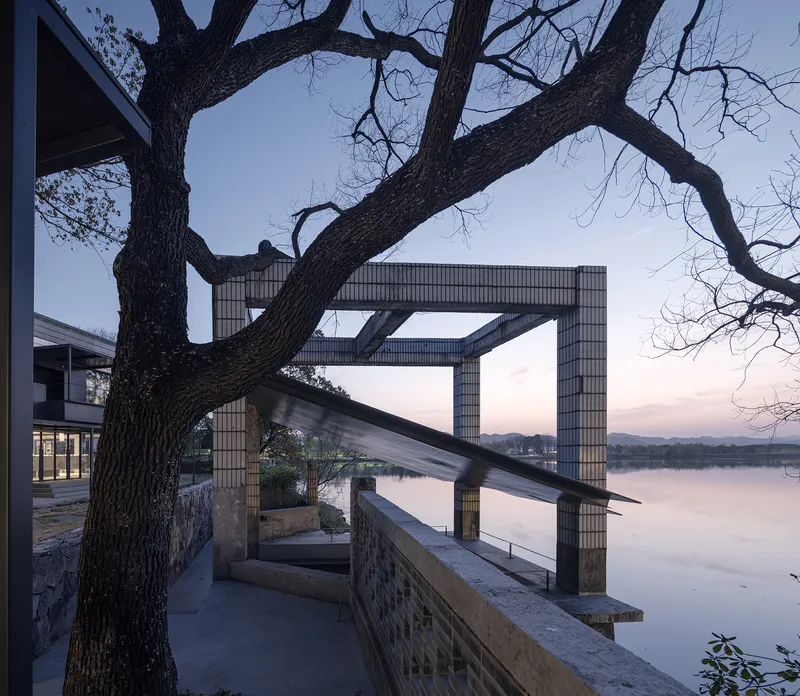 Brick framed portal structure silhouetted against the lake at twilight beneath a bare tree