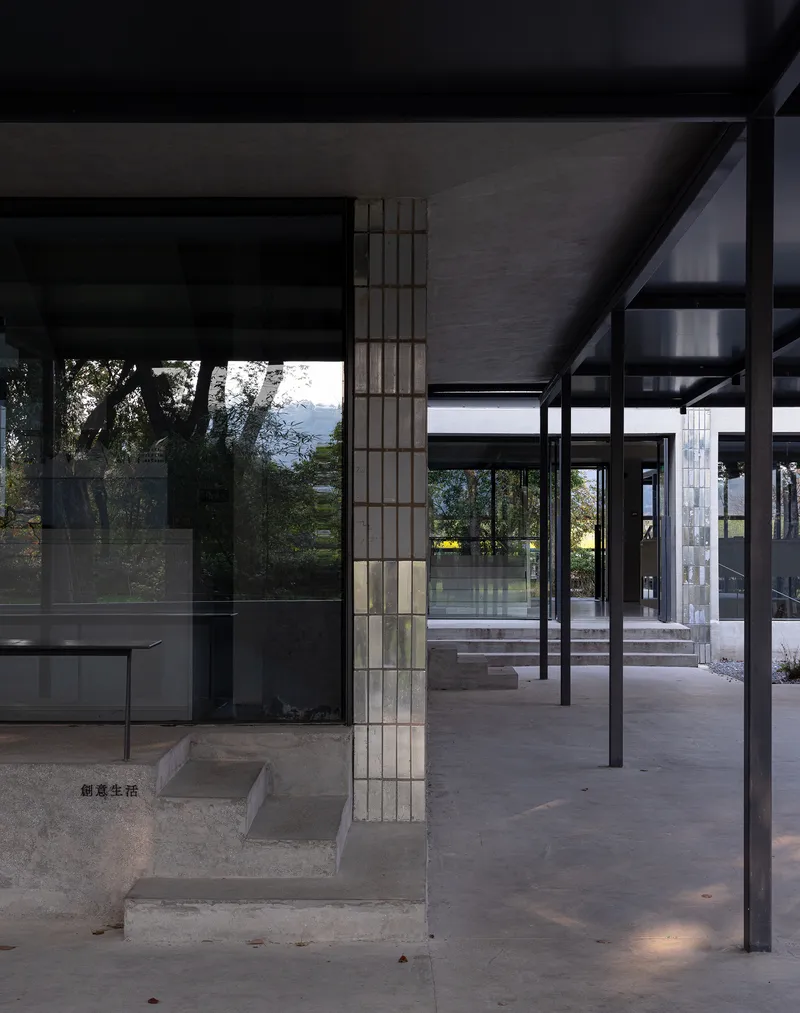 Covered walkway with steel columns and deep overhang framing views of trees and a distant water body