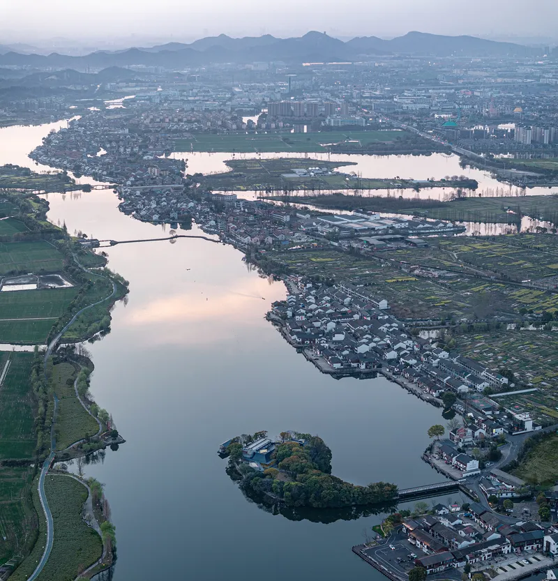 Aerial view of lake with small wooded island and surrounding agricultural fields and settlements at twilight