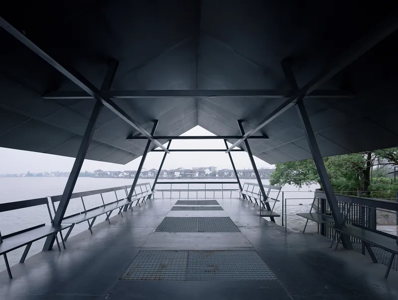 Covered platform with diagonal steel bracing and folded ceiling panels framing a view of the lake