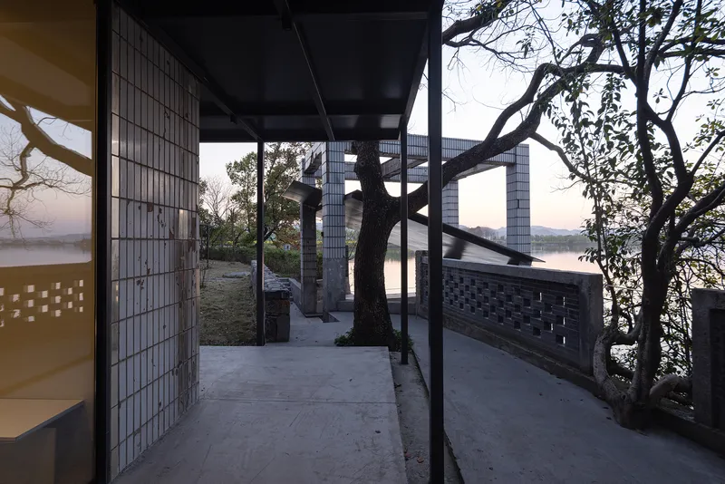 Exterior terrace framed by steel columns and glass block walls with preserved trees at dusk