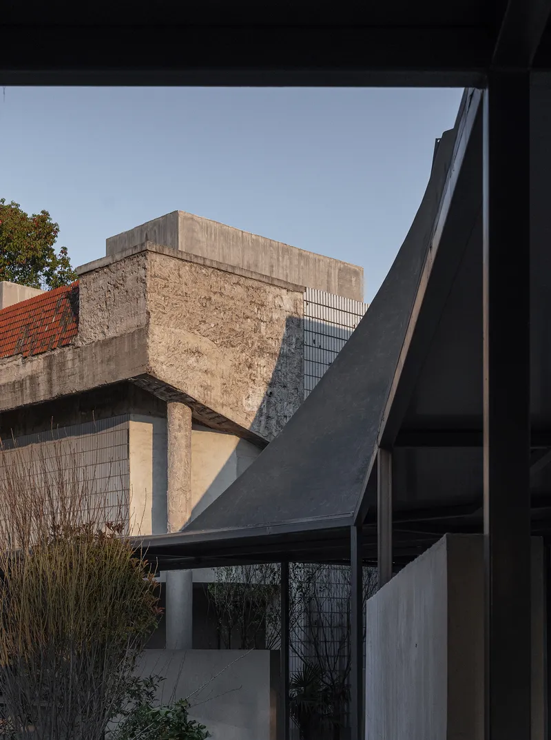 Framed view of exposed concrete bridge remnant and angular roof forms from within the pavilion