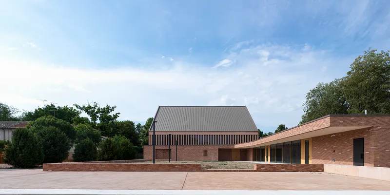 Side view of the gabled roof and low brick wings surrounded by trees under cloud