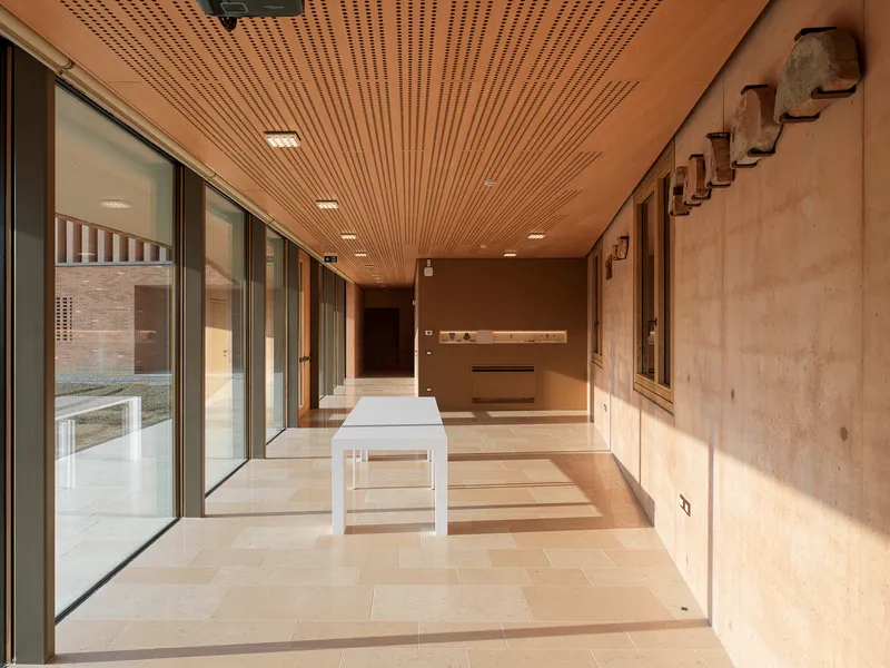 Covered corridor with slatted wood ceiling, glazed walls and limestone flooring in afternoon light