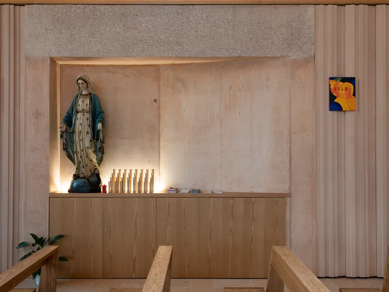 Niche in concrete wall with religious statue, candles and timber cabinetry below