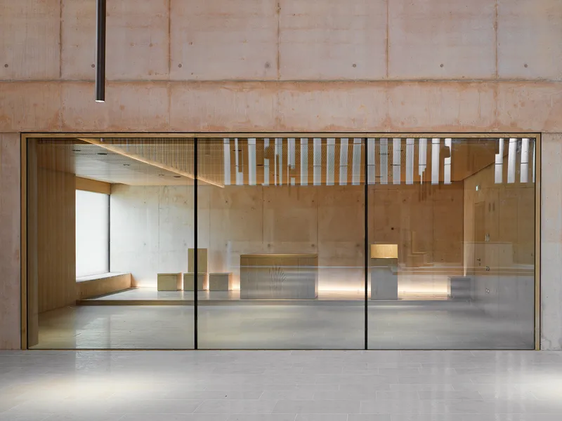 Glass partition framing view into sanctuary with concrete walls and uplighting beneath altar platform
