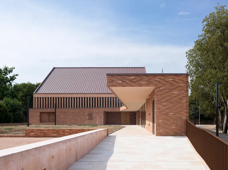 Entrance approach with a cantilevered canopy leading through brick walls and vertical timber screens