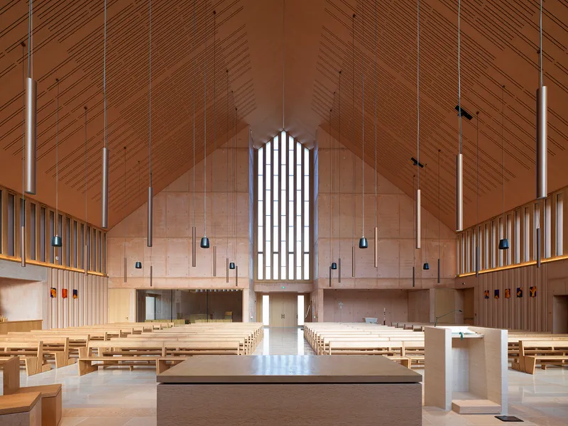 Interior sanctuary with timber-clad pitched ceiling, pendant lights and an arched window above the altar