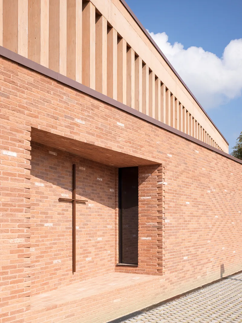 Detail of brick wall with recessed timber cross beside a narrow entrance opening in daylight
