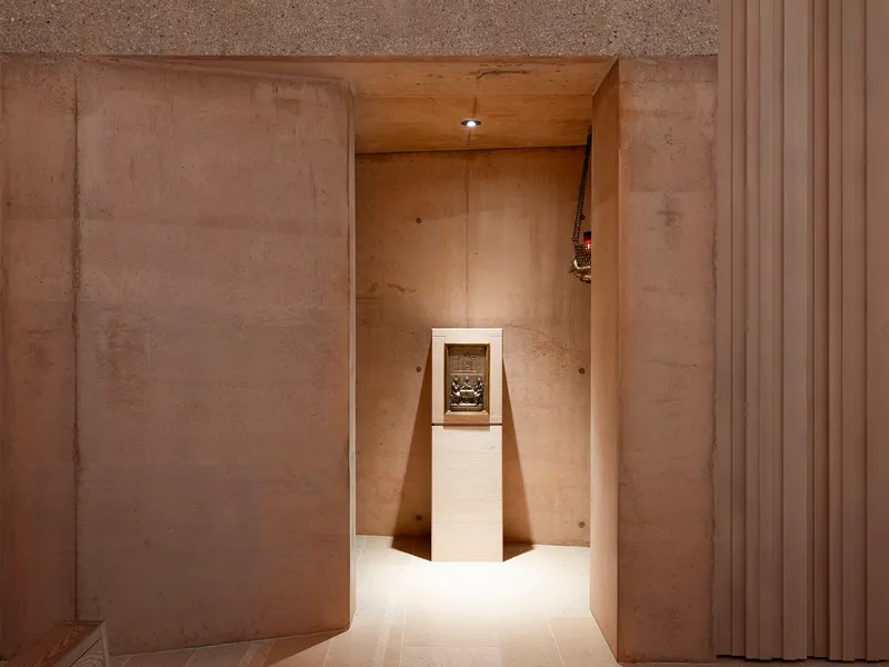 Narrow plywood-lined alcove with a white pedestal displaying a framed artifact under recessed lighting