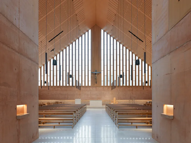 Sanctuary interior with wooden pews facing a vertical slatted window wall and timber ceiling panels