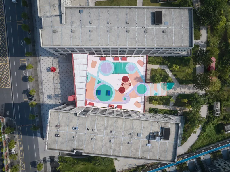 Drone view of the painted rooftop play area wedged between two concrete residential buildings with greenery