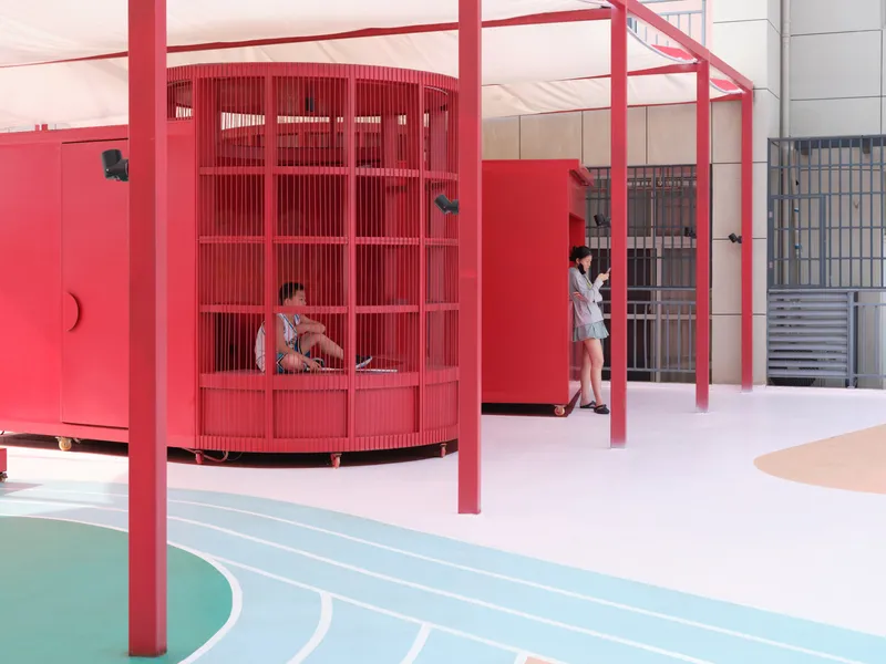Covered courtyard showing cylindrical red storage pavilion with vertical slats beneath steel frame
