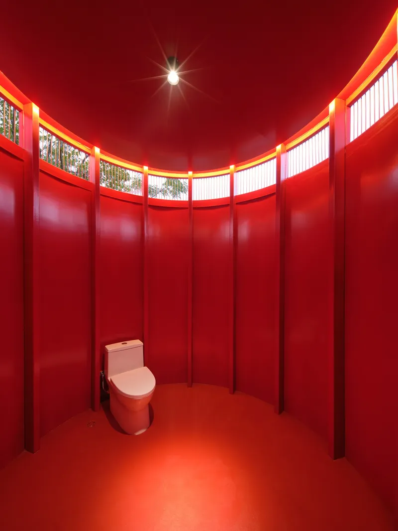 Circular restroom interior with red corrugated wall panels and clerestory band wrapping the curved ceiling