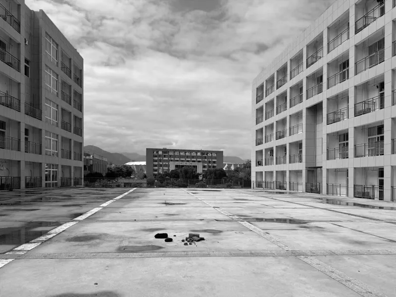 View across the wet concrete plaza toward surrounding residential blocks and distant mountains under cloudy skies