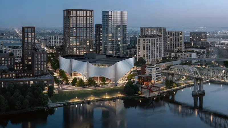 Aerial view of the sculptural roof nestled among residential towers along a riverfront at twilight