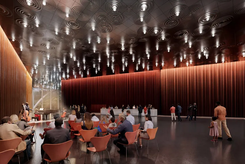 Performance hall foyer with sculptural ceiling panels, pendant lights, and visitors gathered around coral-colored seating