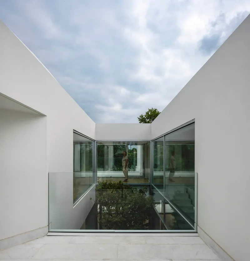 Glass-floored bridge spanning the sunken courtyard between white rendered walls open to the sky