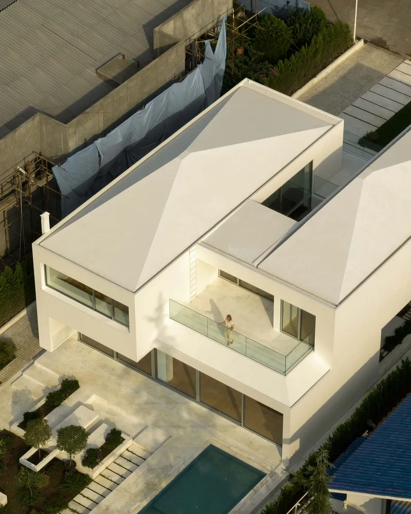 Aerial view of the angular white volumes with folded roof planes and second-floor terrace in afternoon light