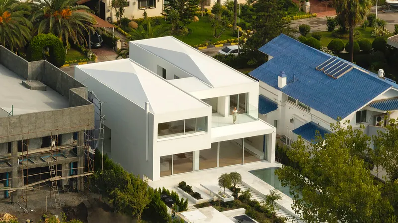 Elevated view of the white stucco facade with ribbon windows and asymmetric roof forms among palm trees
