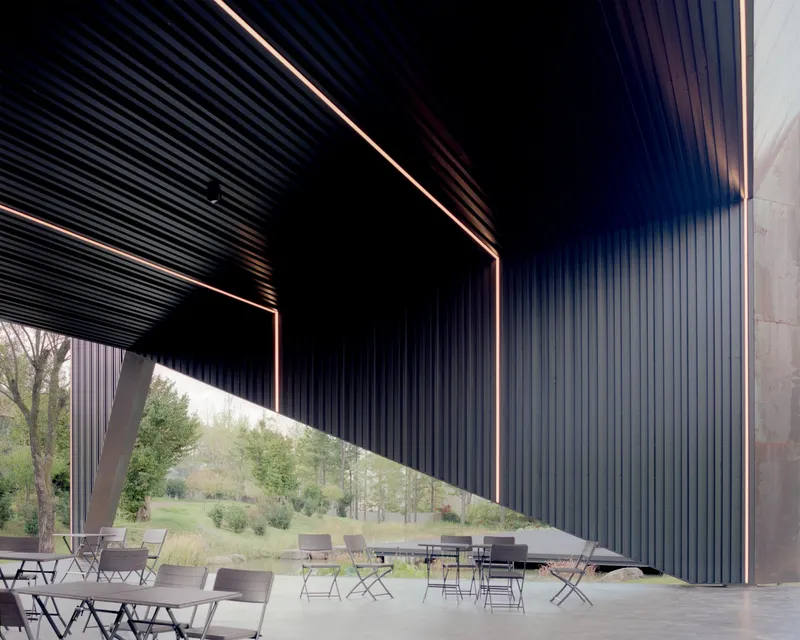 Covered terrace with corrugated metal ceiling and angled columns framing a lawn and distant hills