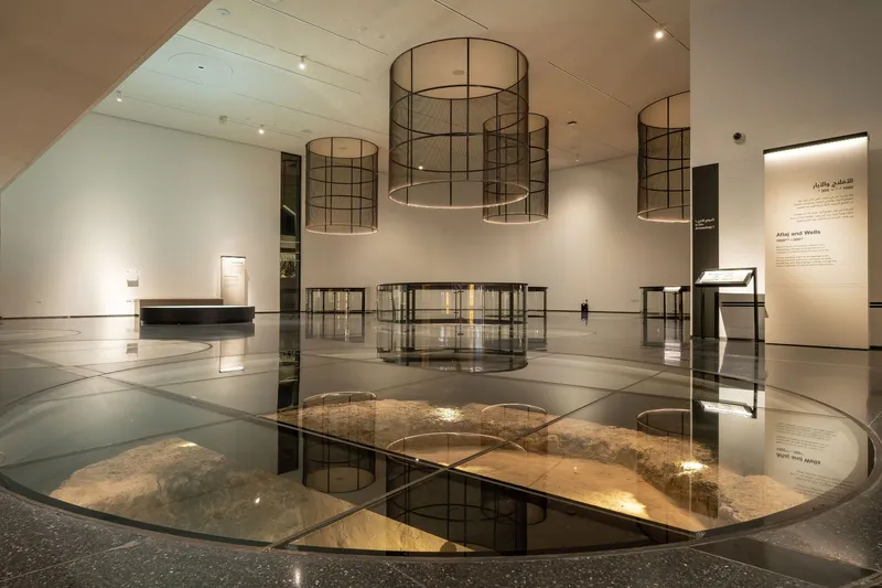 Interior gallery space with circular glass floor panels revealing illuminated archaeological remains below