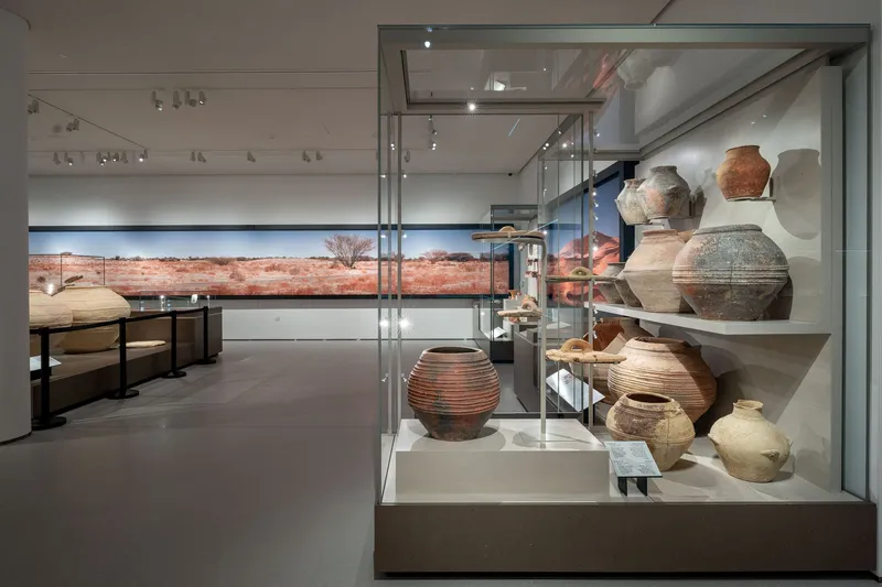 Glass display cases holding ceramic vessels with desert landscape visible through horizontal window