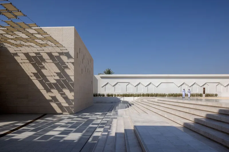 Courtyard with wide stone steps and a perforated timber canopy casting geometric shadows in midday sun