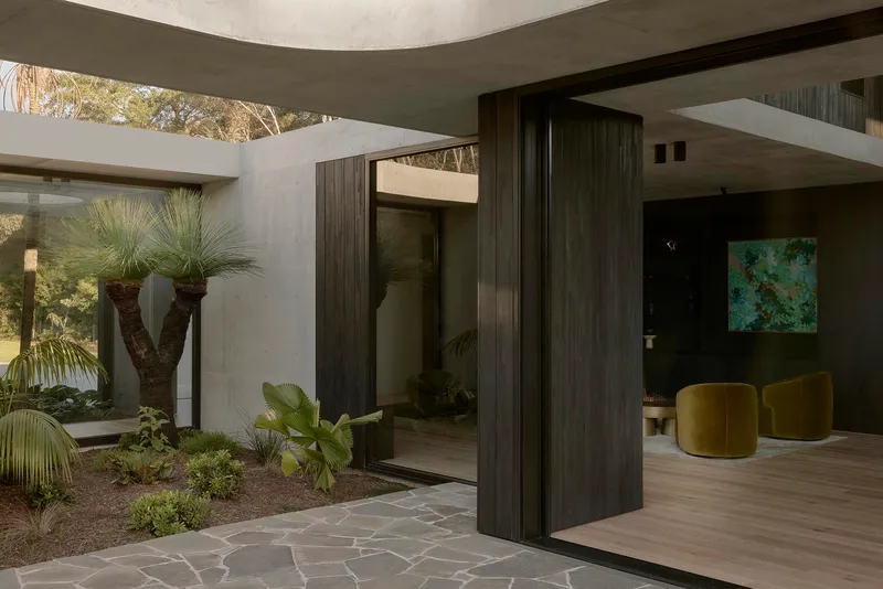 Entry threshold with pivoting timber door opening to planted courtyard beneath concrete soffit
