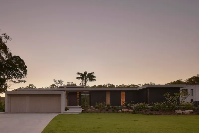 Garden elevation with horizontal roofline and planted beds at dusk beneath a palm tree