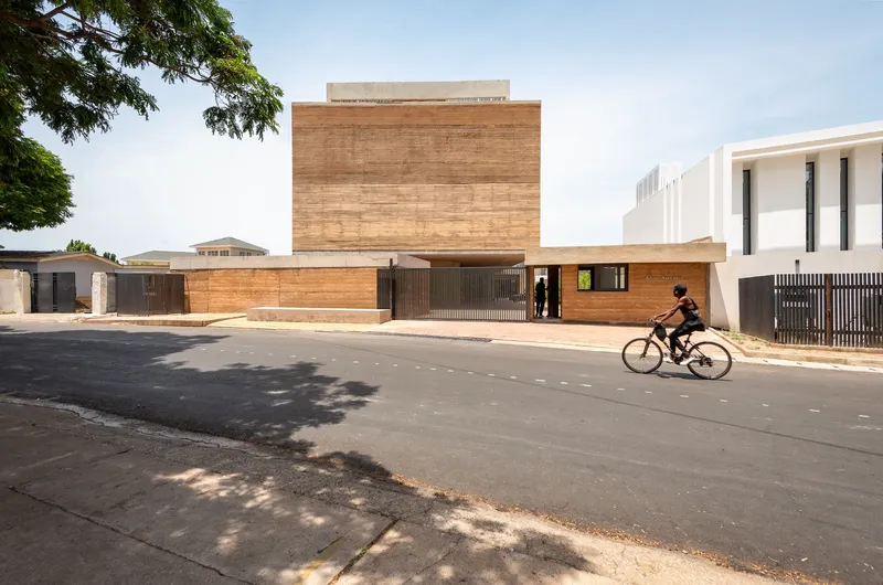 Street view of the layered timber facade with a cyclist passing in afternoon light