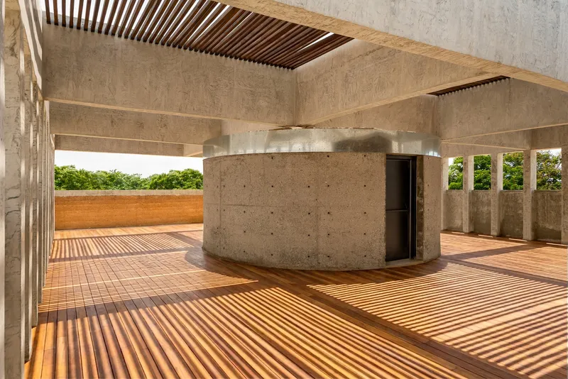 Rooftop terrace with timber slat flooring, slatted ceiling, curved concrete core, and view to greenery