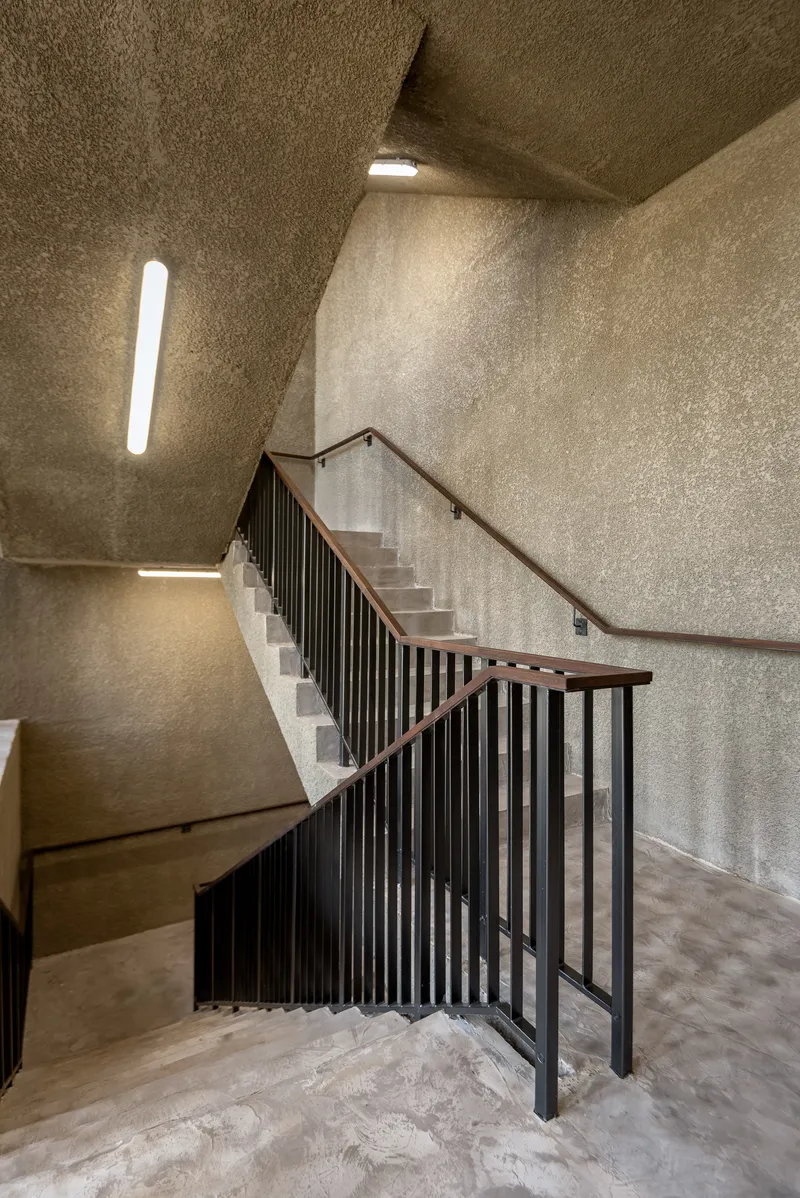 Concrete stairwell with metal railing and narrow vertical skylights illuminating the textured walls