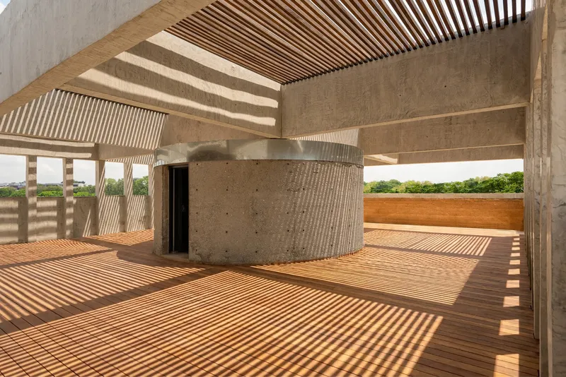 Rooftop terrace with timber decking and slatted pergola casting striped shadows across rammed earth walls