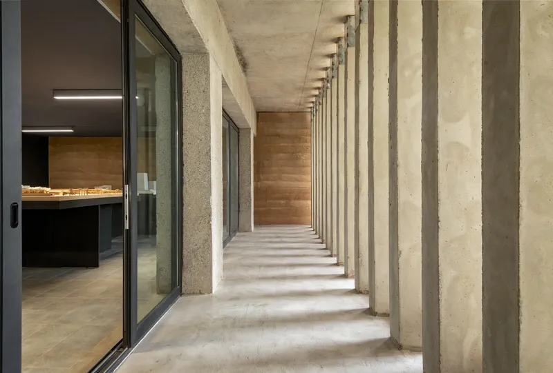 Covered walkway with rhythmic concrete columns casting shadows along the polished concrete floor