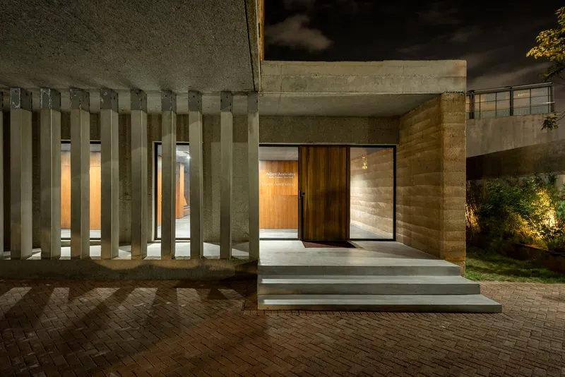 Night view of the entrance with vertical concrete fins and timber pivot door above brick pavers