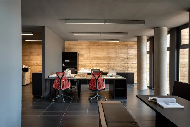 Open office space with red mesh chairs at black desks beneath recessed linear ceiling lights