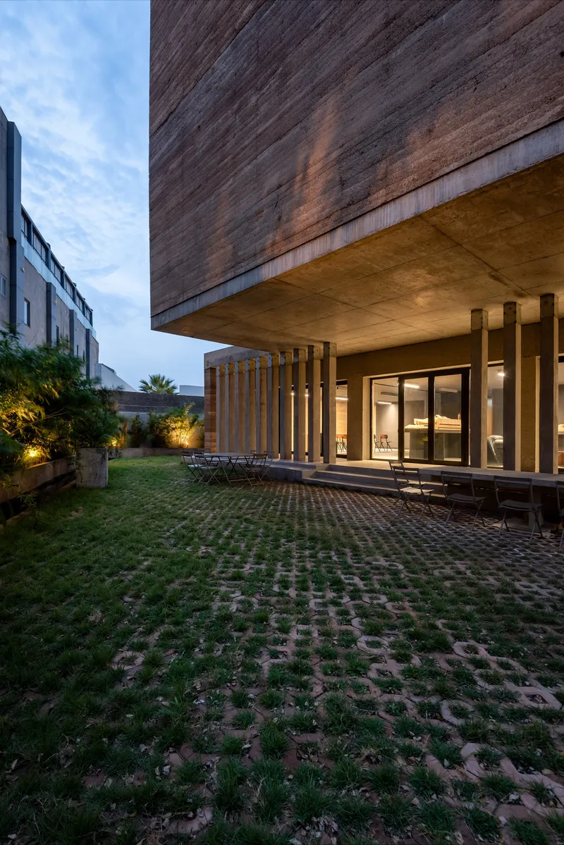 Courtyard view of the cantilevered timber-clad volume above a colonnade at dusk