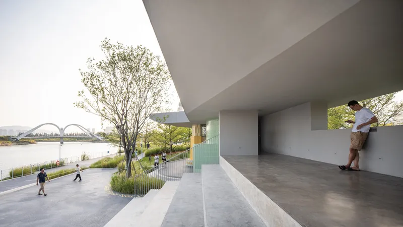 Covered terrace with concrete soffit overlooking a riverside promenade with pedestrians and trees