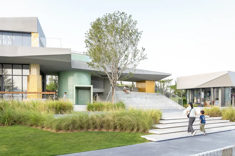 Wide steps ascending through landscaped grass beds toward the elevated terrace with glazed facade