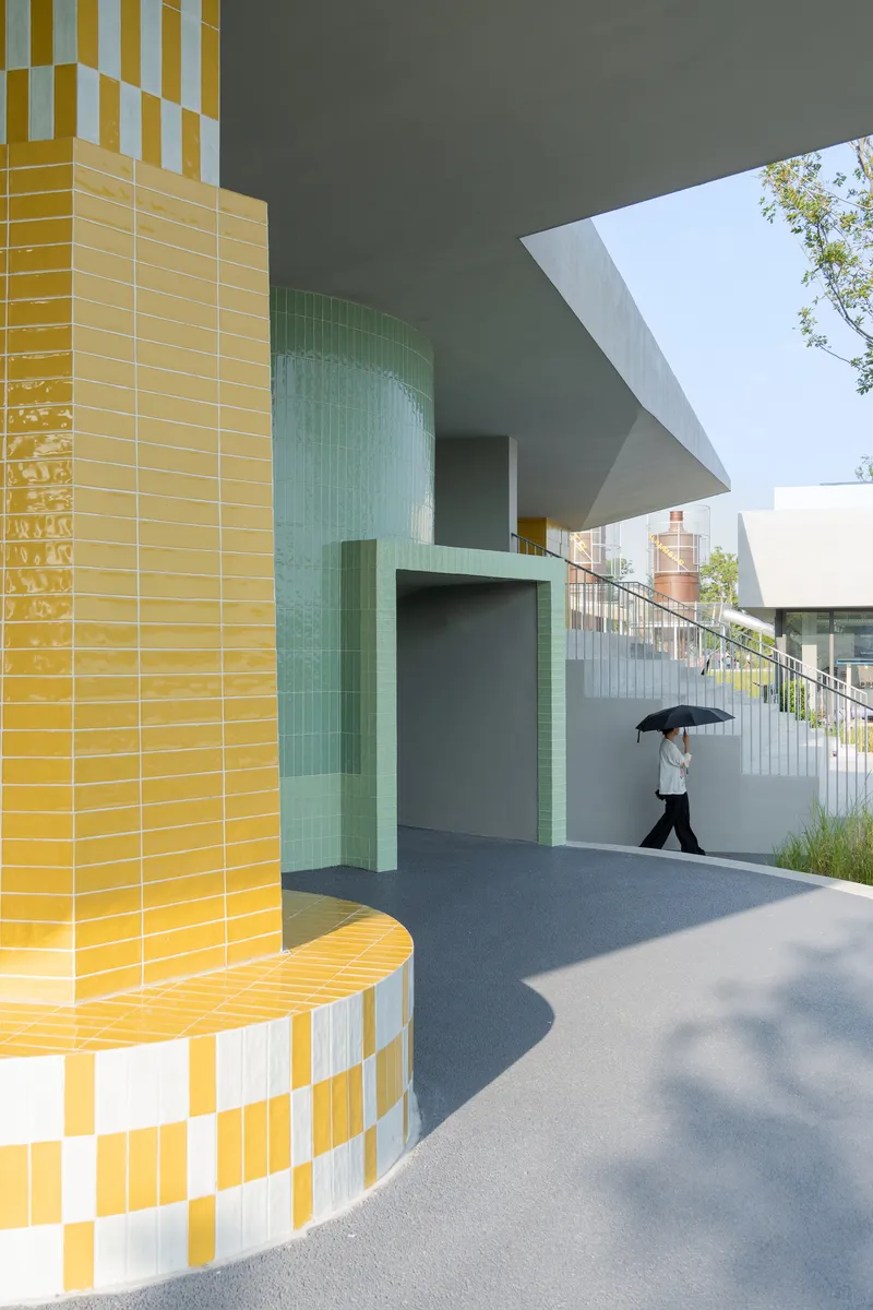 Recessed entrance portal clad in mint green tile with a figure carrying an umbrella