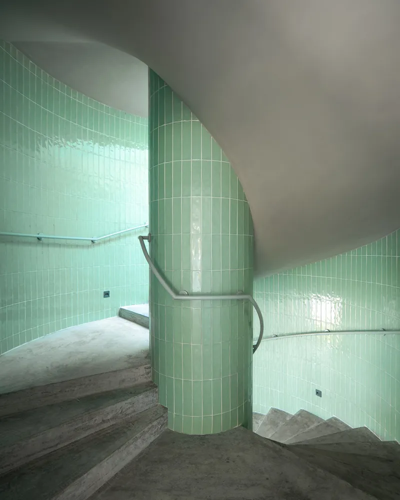 Curved stairwell wrapped in pale green subway tile with concrete treads and metal handrail