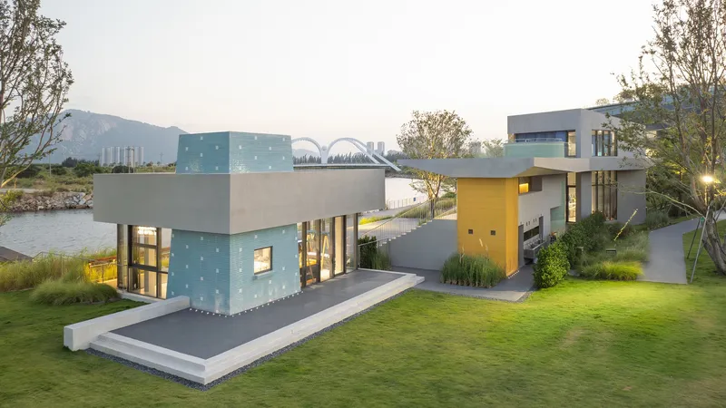 Elevated view of the waterside complex with green glass block volume and yellow entrance pavilion at dusk