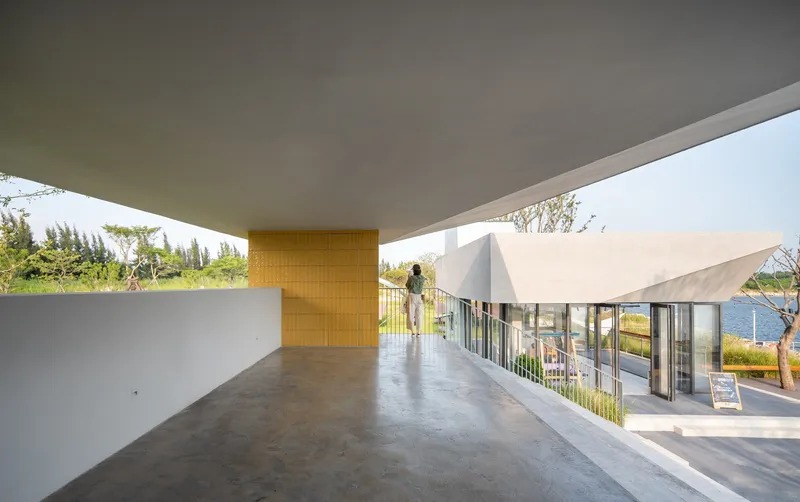 Covered terrace with concrete soffit and yellow tiled column overlooking the lawn and water with a figure