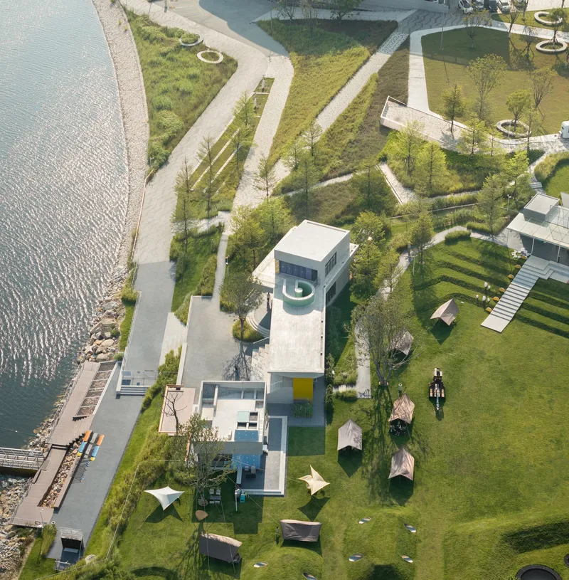 Aerial view of white pavilions surrounded by curved terraced lawn and waterfront dock with kayakers