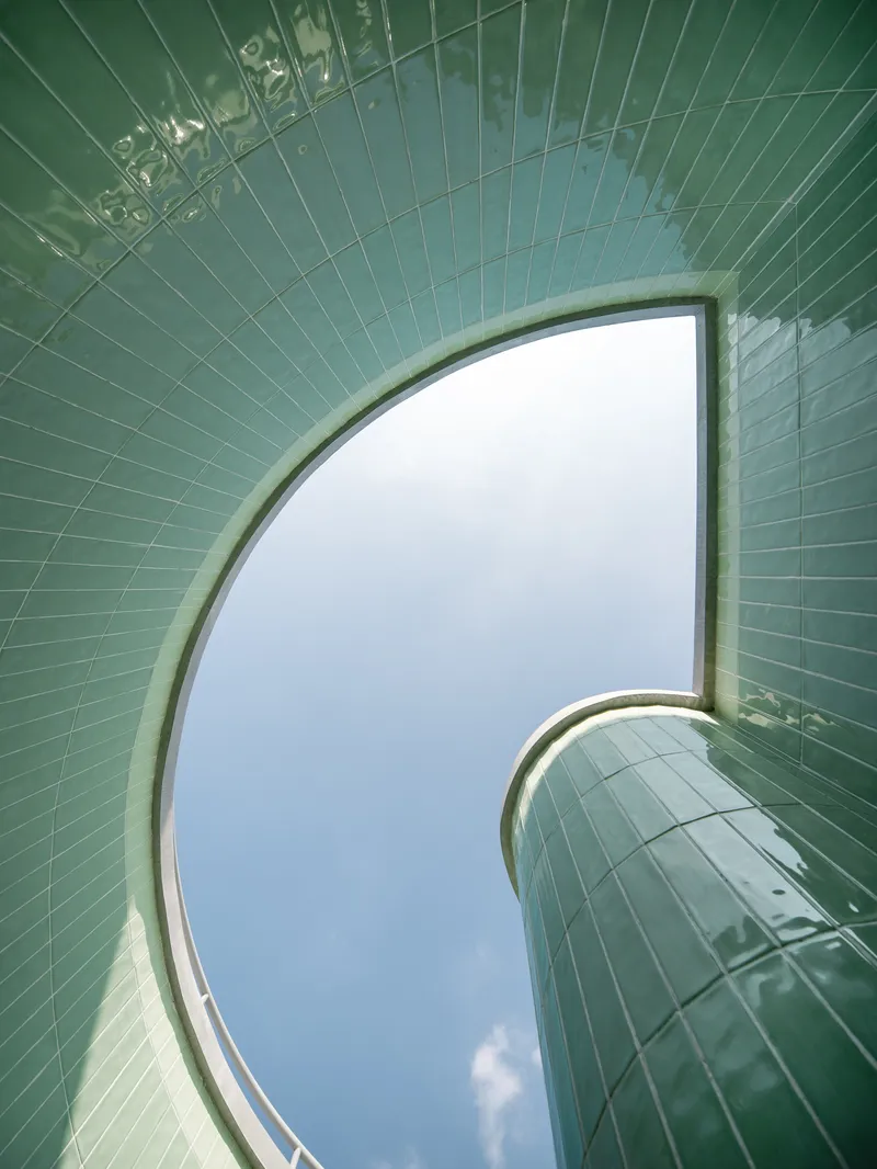 Upward view through curved green-tiled skylight opening framing a patch of overcast sky