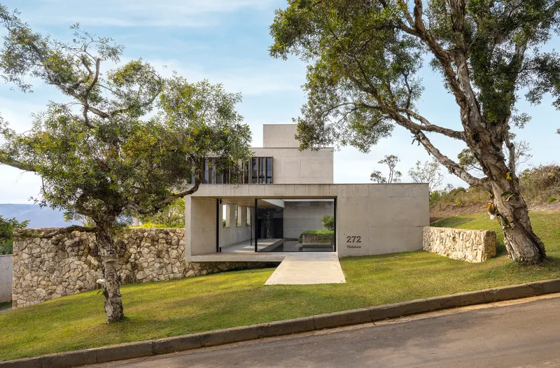 Street view of the concrete volume entrance flanked by gabion stone walls and mature trees