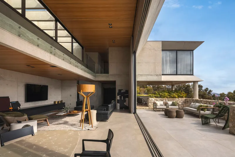 Double height living space opening to a terrace with hillside views under concrete soffits