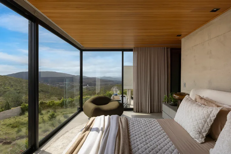 Bedroom with floor-to-ceiling glazing and timber ceiling overlooking distant hills